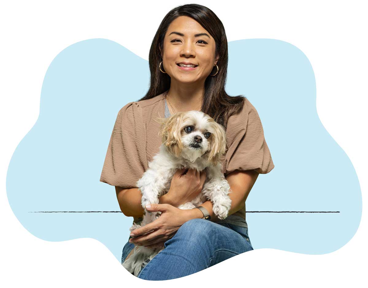 A woman in a brown shirt sitting with her white dog in her lap